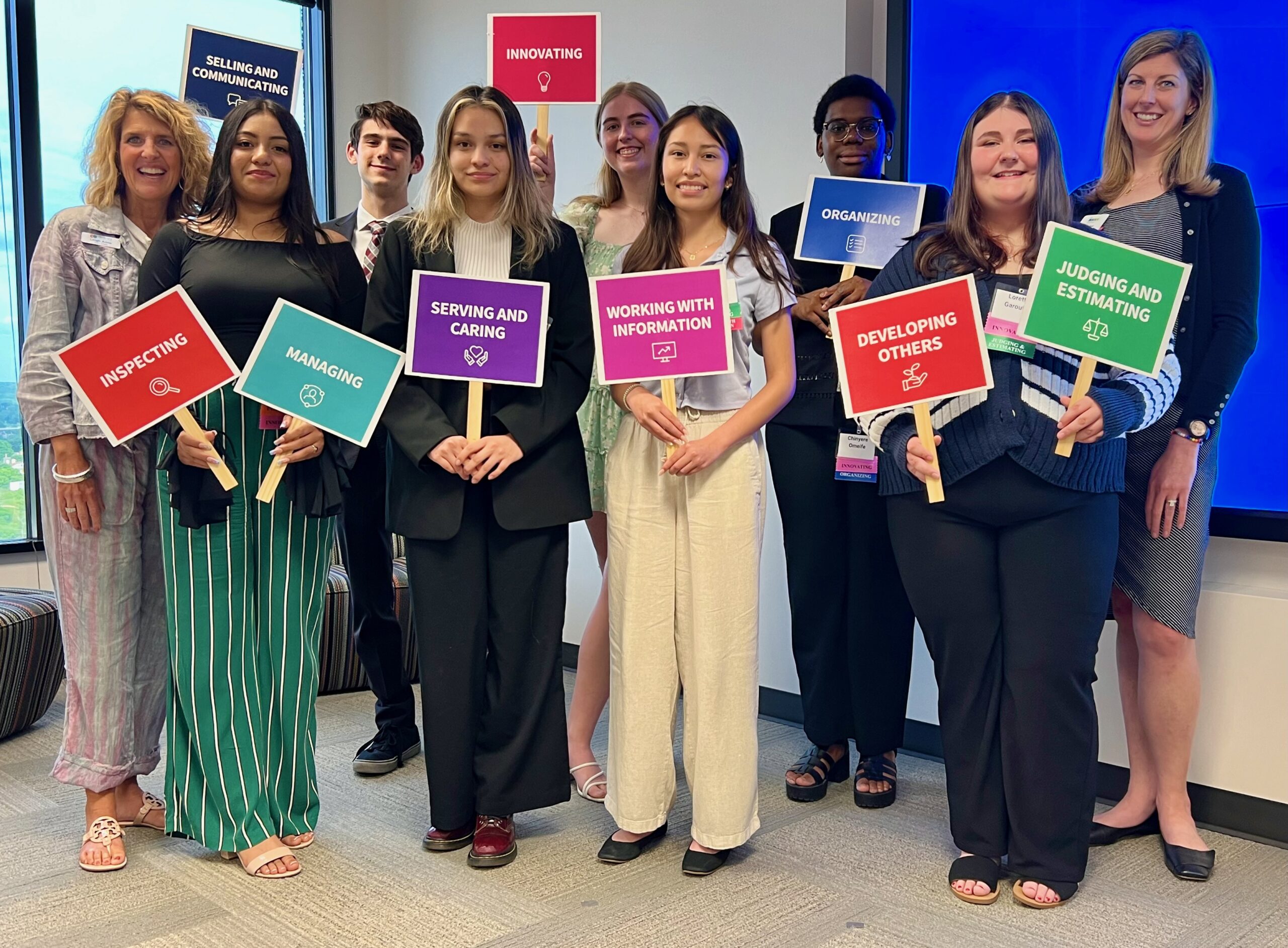 Recipients of the 2024 Make It REAL Scholarship pose with Leigh Ann Taylor Knight of The DeBruce Foundation and Chelsea Barbercheck of the KC STEM Alliance. They are each holding a colorful sign illustrating their top Agility.